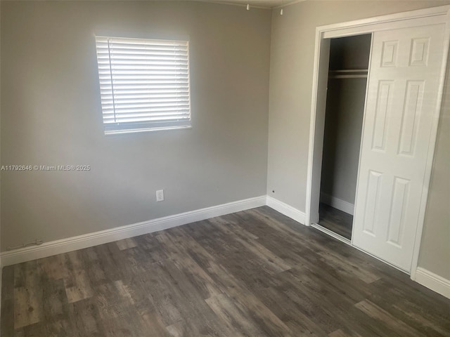 unfurnished bedroom with baseboards, dark wood-style floors, and a closet