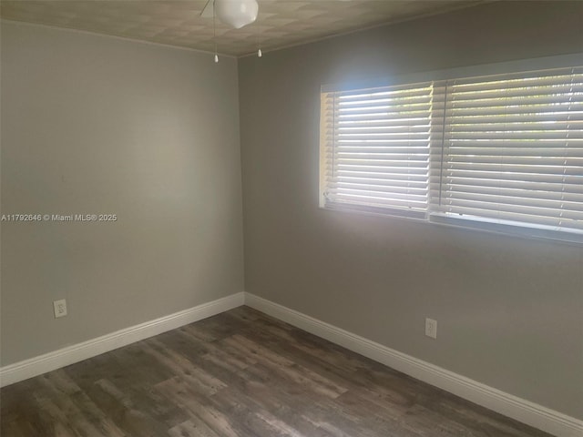 empty room with crown molding, baseboards, and dark wood finished floors