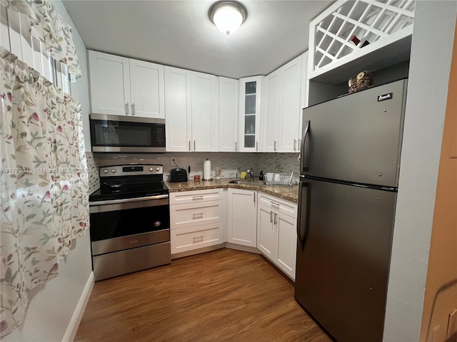 kitchen featuring a sink, stainless steel appliances, white cabinetry, wood finished floors, and glass insert cabinets