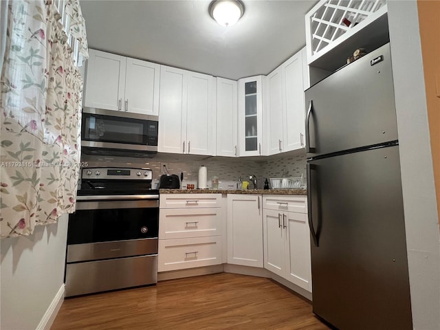 kitchen with baseboards, white cabinets, light wood finished floors, glass insert cabinets, and stainless steel appliances