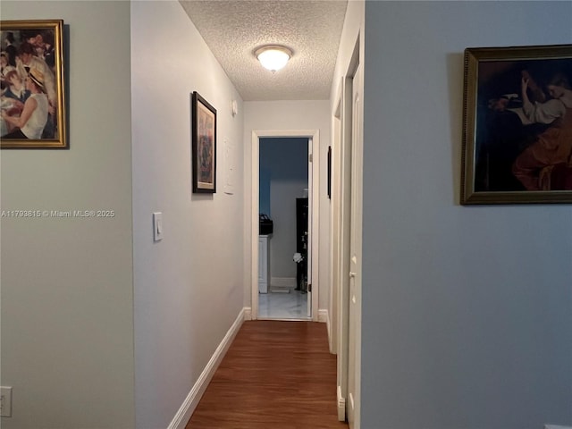 hallway with baseboards, a textured ceiling, and wood finished floors