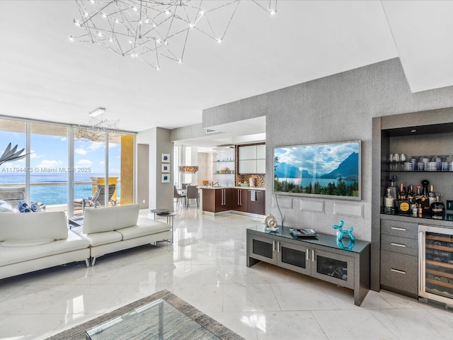 living area with a dry bar, marble finish floor, beverage cooler, a notable chandelier, and a water view