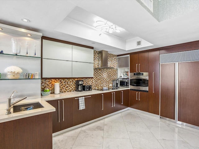 kitchen featuring oven, a raised ceiling, wall chimney exhaust hood, paneled built in refrigerator, and a sink