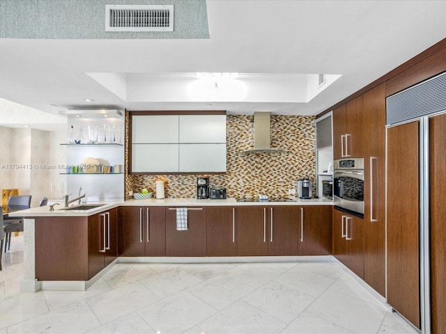 kitchen with wall chimney range hood, a tray ceiling, a peninsula, and oven