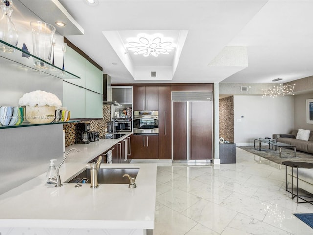 17875 Collins Ave Unit 1605, Sunny Isles Beach, FL 33160 - kitchen featuring appliances with stainless steel finishes, wall chimney exhaust hood, a raised ceiling, tasteful backsplash, and dark brown cabinetry