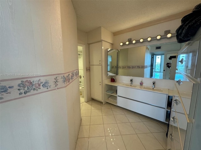 full bath with a sink, double vanity, a textured ceiling, and tile patterned floors