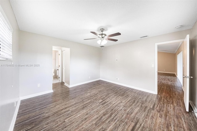 unfurnished room featuring visible vents, baseboards, ceiling fan, and dark wood-style floors