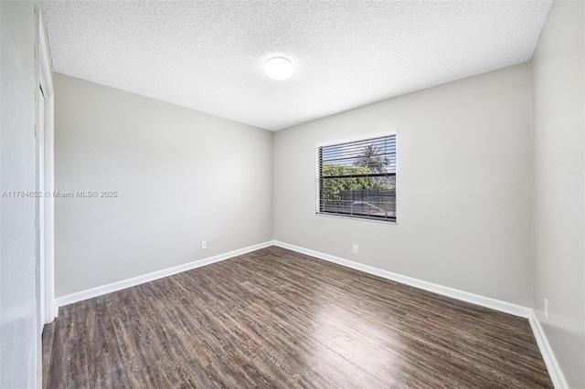 spare room with baseboards, dark wood-style floors, and a textured ceiling