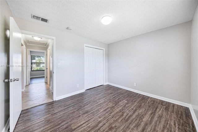 unfurnished bedroom featuring visible vents, a closet, baseboards, a textured ceiling, and dark wood finished floors