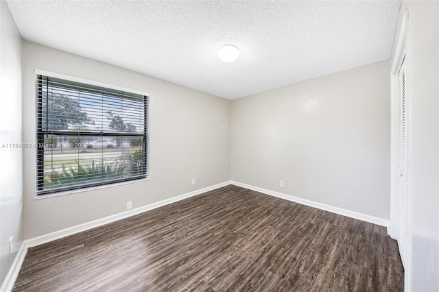 empty room featuring dark wood-style flooring, a textured ceiling, and baseboards