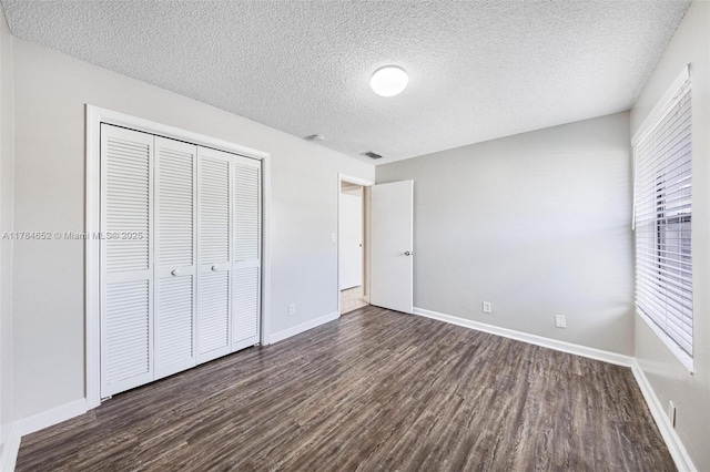 unfurnished bedroom with a closet, a textured ceiling, dark wood finished floors, and baseboards