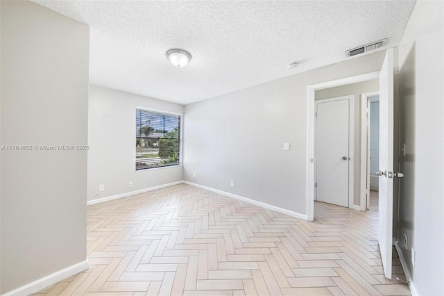 unfurnished room with visible vents, a textured ceiling, and baseboards