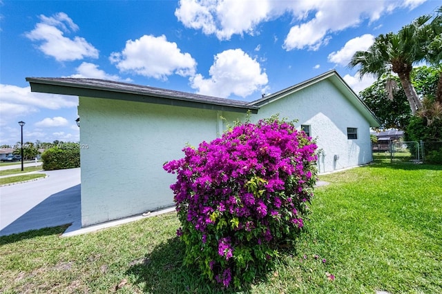 view of side of home featuring a lawn, stucco siding, and fence