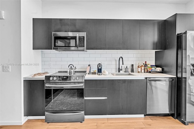 kitchen with appliances with stainless steel finishes, a sink, light countertops, decorative backsplash, and light wood-type flooring