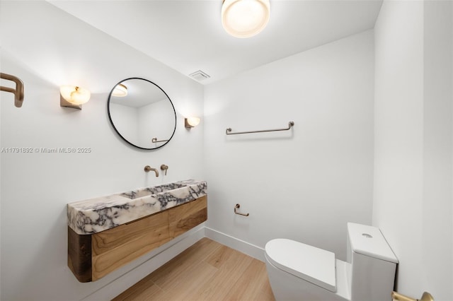 bathroom with vanity, toilet, baseboards, wood finished floors, and visible vents