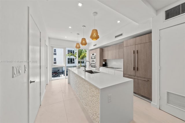 kitchen with a sink, light countertops, an island with sink, visible vents, and modern cabinets