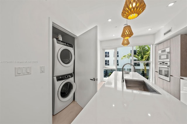 clothes washing area featuring a sink, stacked washer / drying machine, recessed lighting, and visible vents