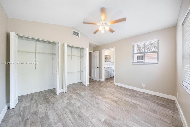 unfurnished bedroom featuring light wood-style flooring, two closets, baseboards, vaulted ceiling, and visible vents