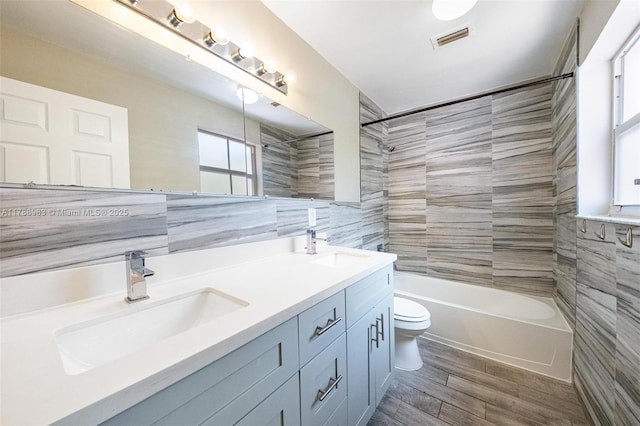 bathroom with visible vents, wood finished floors, toilet, tile walls, and a sink