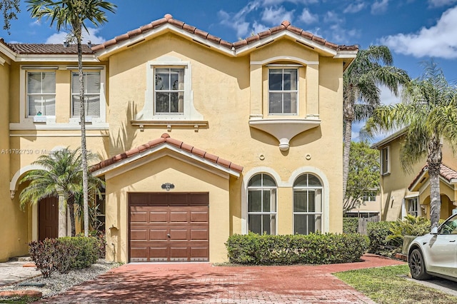 mediterranean / spanish home featuring a tiled roof, an attached garage, decorative driveway, and stucco siding