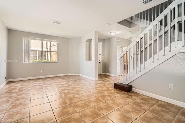 interior space featuring baseboards, light tile patterned floors, visible vents, and stairway