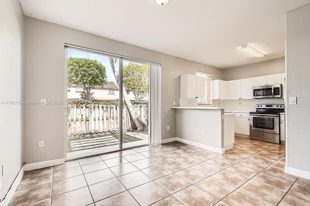 kitchen with a peninsula, light countertops, white cabinets, appliances with stainless steel finishes, and light tile patterned floors