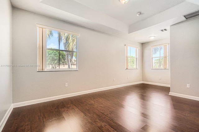 unfurnished room featuring baseboards, visible vents, a tray ceiling, and dark wood-type flooring