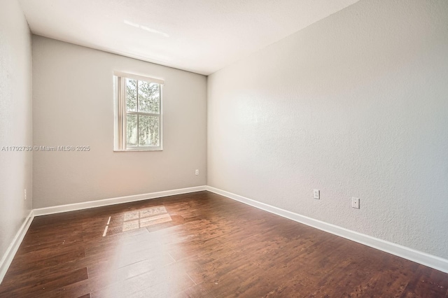 spare room featuring baseboards and dark wood-style floors