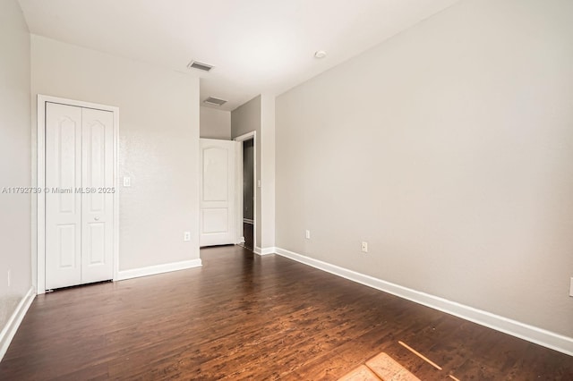 unfurnished bedroom featuring baseboards, a closet, dark wood-style flooring, and visible vents