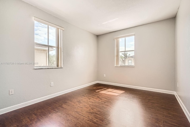 empty room featuring baseboards and dark wood-type flooring