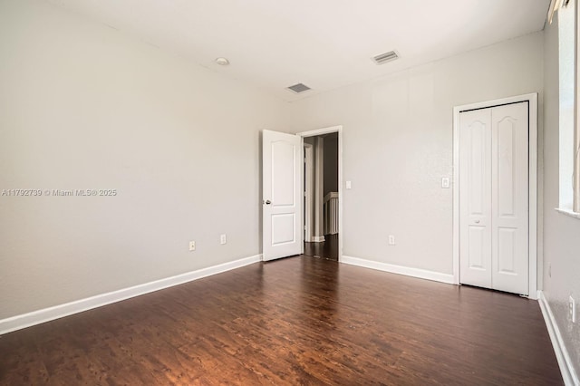unfurnished bedroom featuring a closet, baseboards, visible vents, and dark wood-type flooring