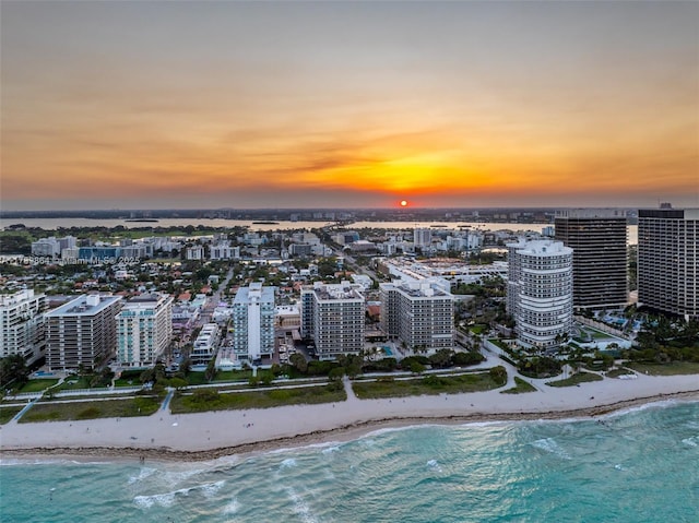 aerial view at dusk featuring a water view, a city view, and a view of the beach
