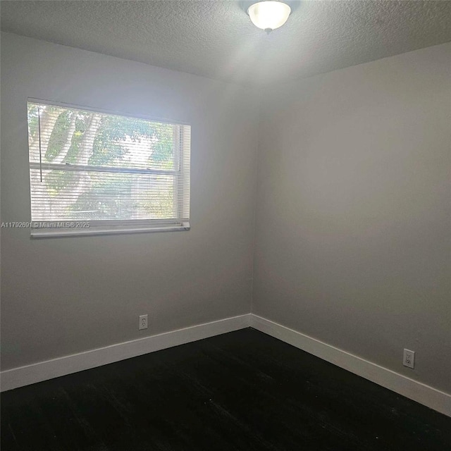 spare room with a textured ceiling, baseboards, and dark wood-style floors