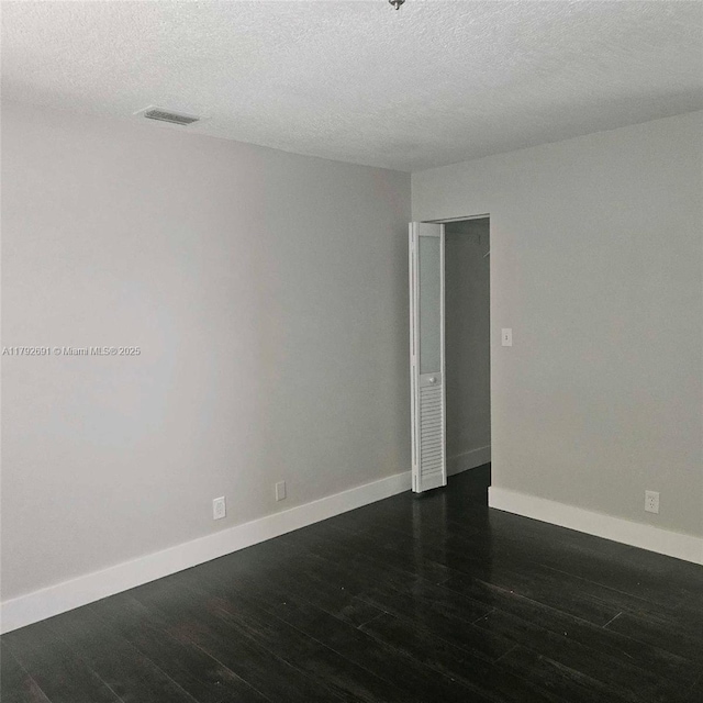 empty room with baseboards, a textured ceiling, and dark wood-style flooring