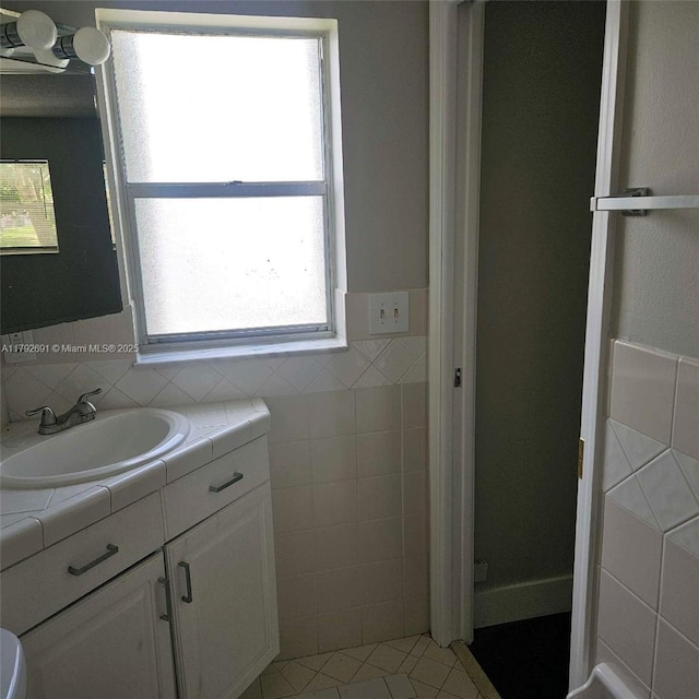 bathroom with a healthy amount of sunlight, vanity, tile patterned floors, and tile walls