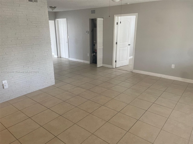 spare room with light tile patterned flooring, brick wall, visible vents, and baseboards