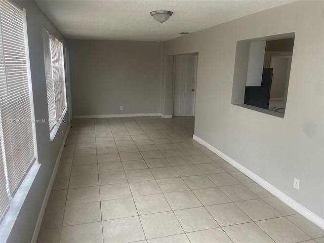 spare room with light tile patterned floors, baseboards, and a wealth of natural light