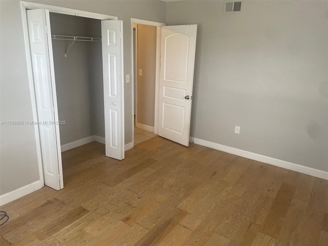 unfurnished bedroom with baseboards, a closet, light wood-type flooring, and visible vents