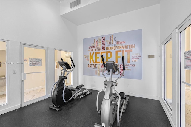 exercise area with baseboards, a high ceiling, and visible vents