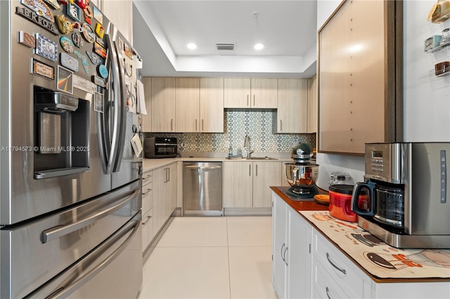 kitchen with decorative backsplash, recessed lighting, a tray ceiling, a sink, and appliances with stainless steel finishes