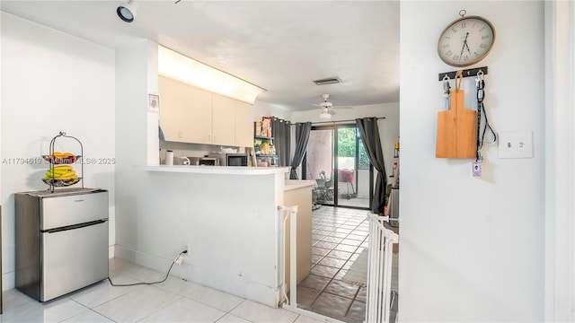 kitchen with freestanding refrigerator, a peninsula, light tile patterned flooring, and visible vents