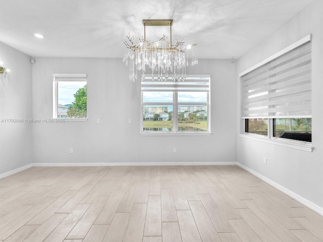 empty room featuring an inviting chandelier, baseboards, wood finished floors, and a healthy amount of sunlight