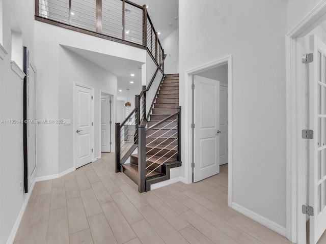 staircase with baseboards, recessed lighting, wood finished floors, and a towering ceiling