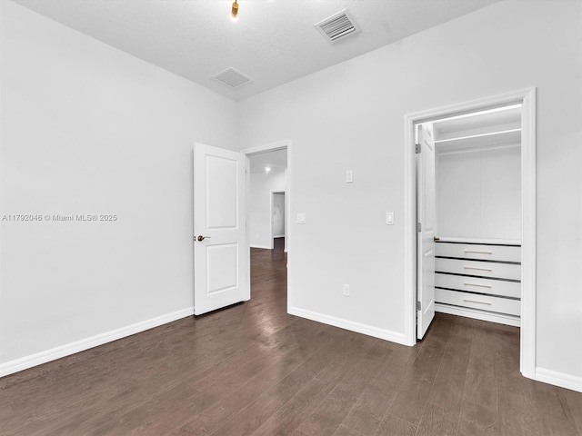 unfurnished bedroom with dark wood-style flooring, baseboards, visible vents, and a walk in closet