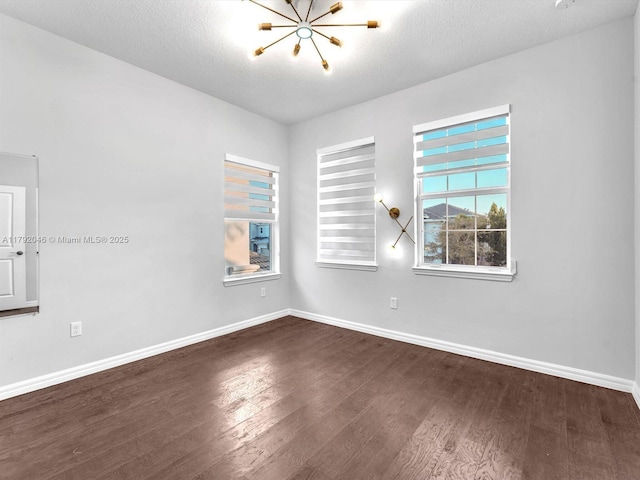 empty room with dark wood-type flooring, baseboards, plenty of natural light, and a notable chandelier