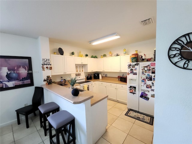 kitchen with a peninsula, light tile patterned flooring, white appliances, and a kitchen bar