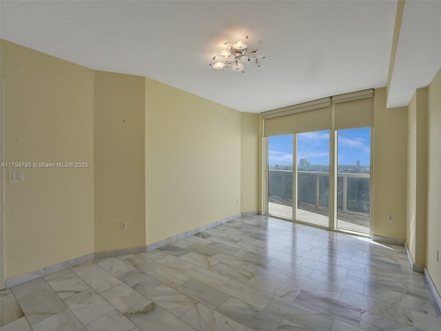 empty room featuring a wall of windows and baseboards