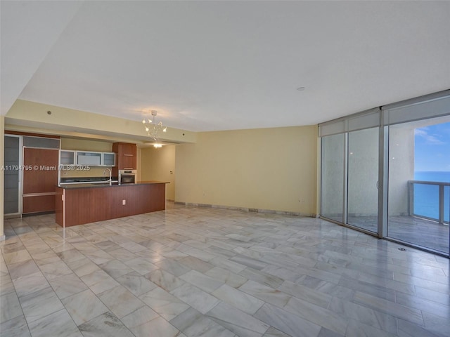 unfurnished living room with a notable chandelier, a wall of windows, a sink, and marble finish floor