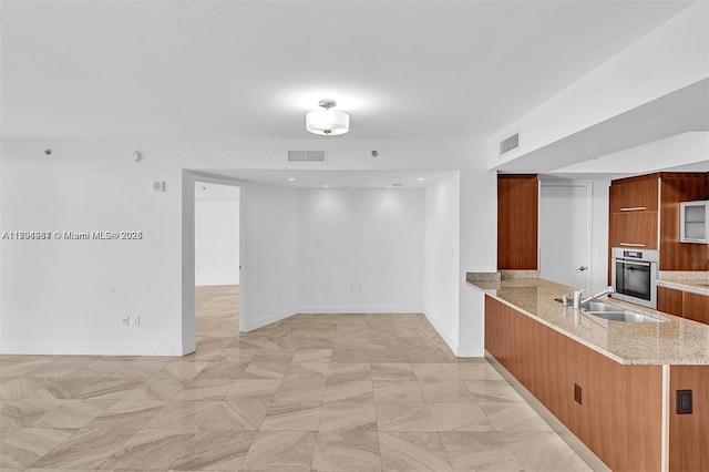 kitchen with a sink, stainless steel oven, brown cabinets, and visible vents