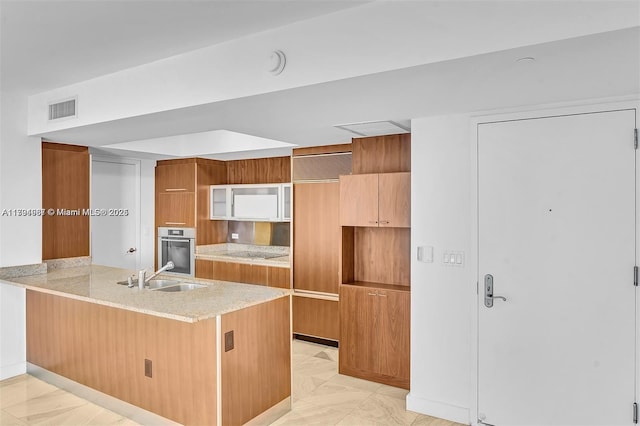 kitchen featuring stainless steel oven, brown cabinetry, modern cabinets, and visible vents